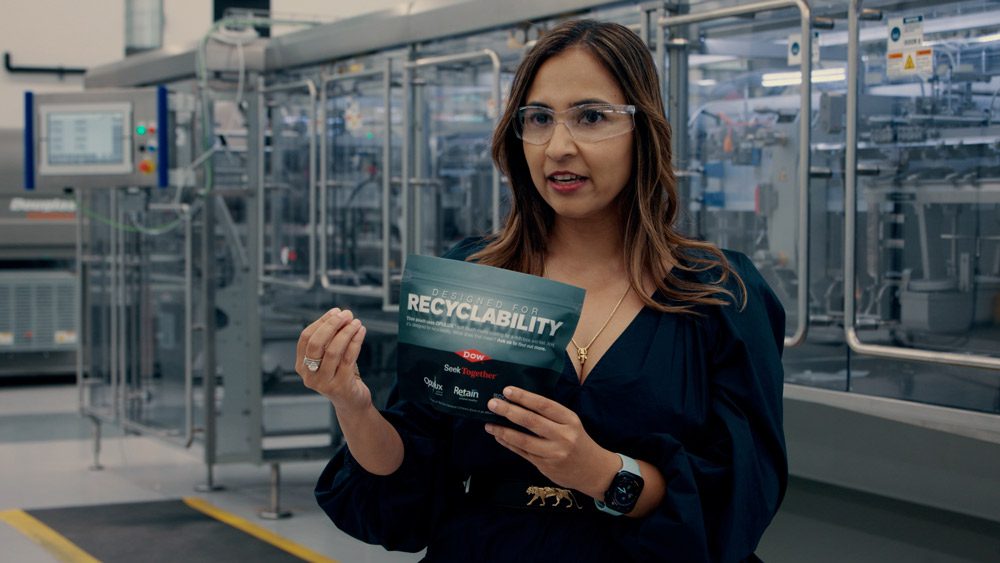 Rashi holding a plastic package that says "Designed for Recyclability".