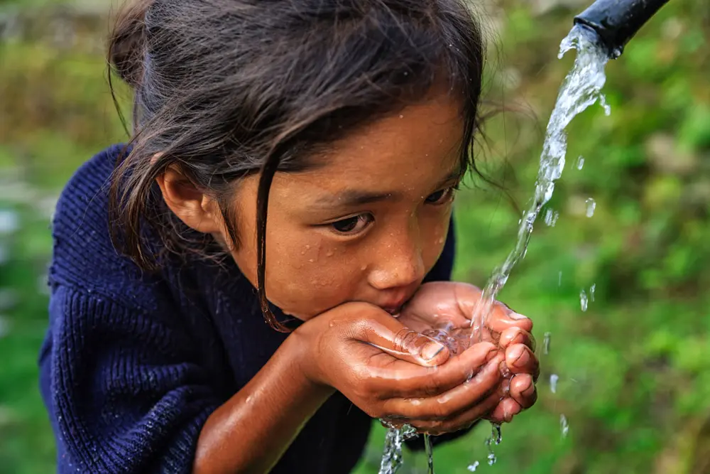 Little girl drinking water from plastic pipe