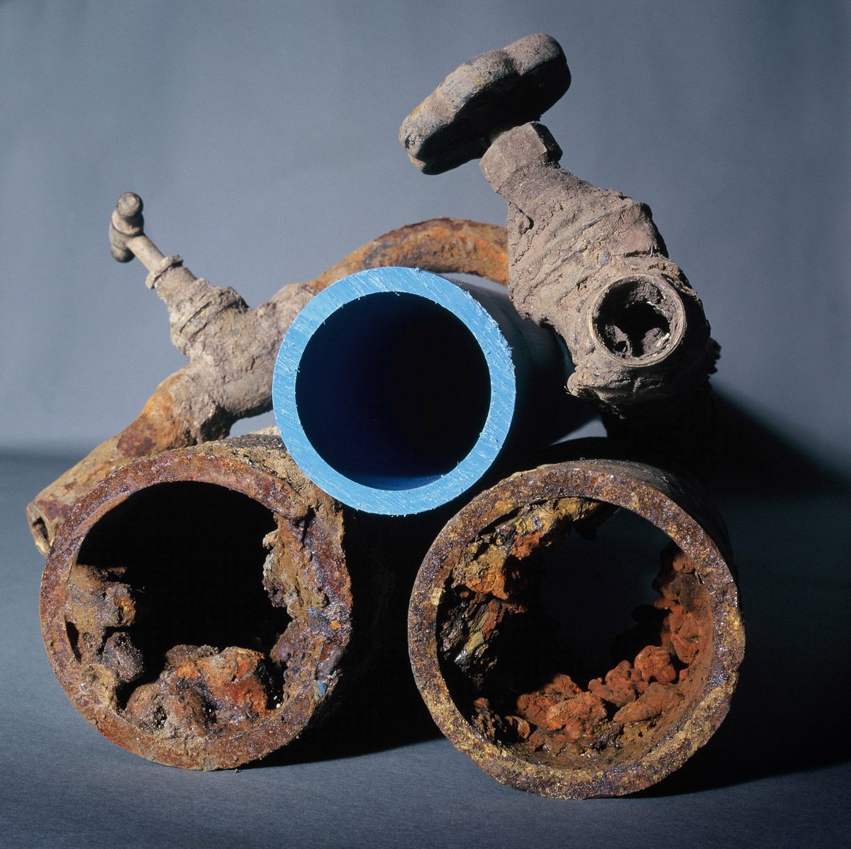 Old corroded rusty metal domestic water pipes alongside a new plastic pipe