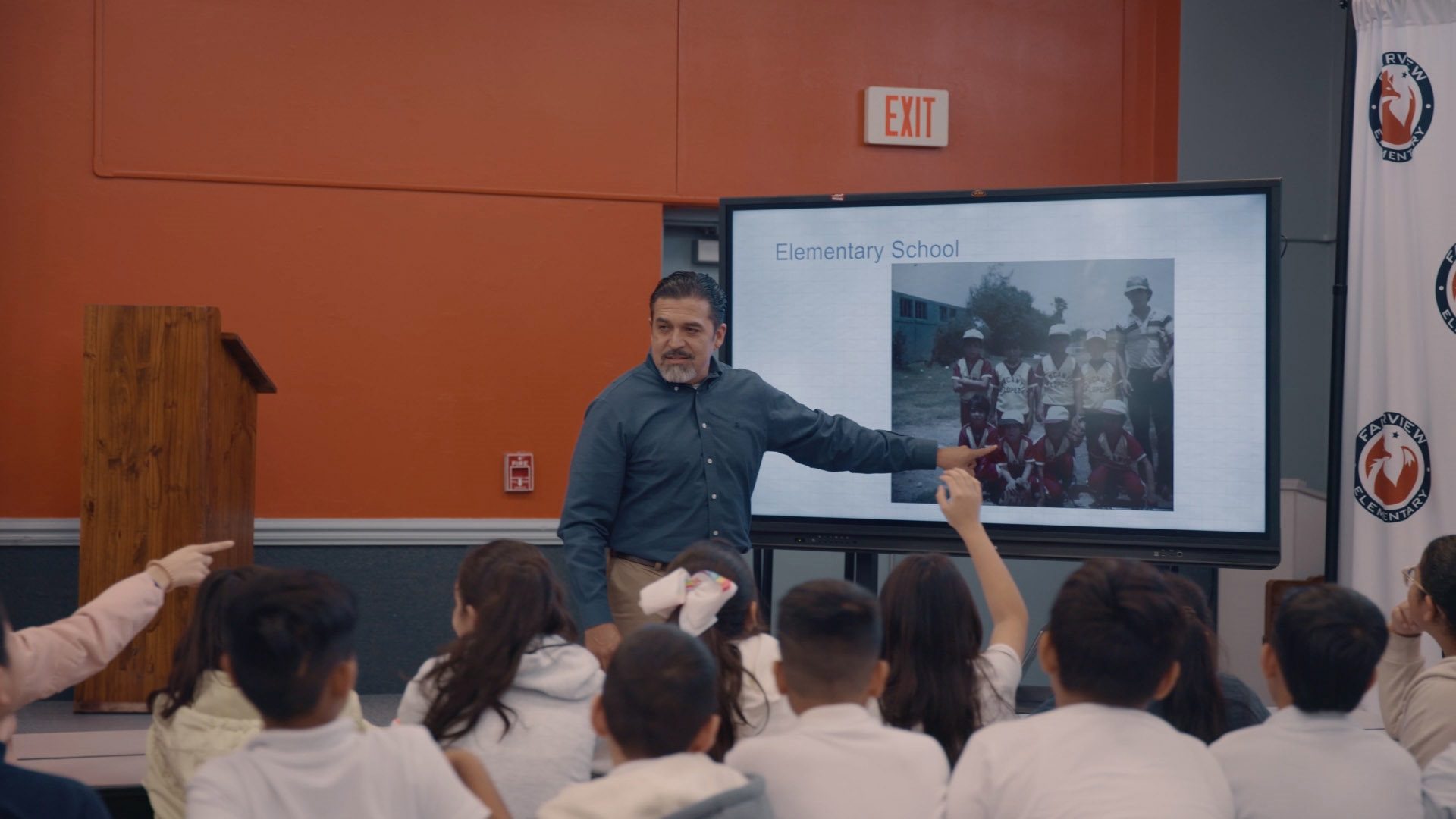 Armando from LDB pointing to a large screen in front of school kids with raised hands