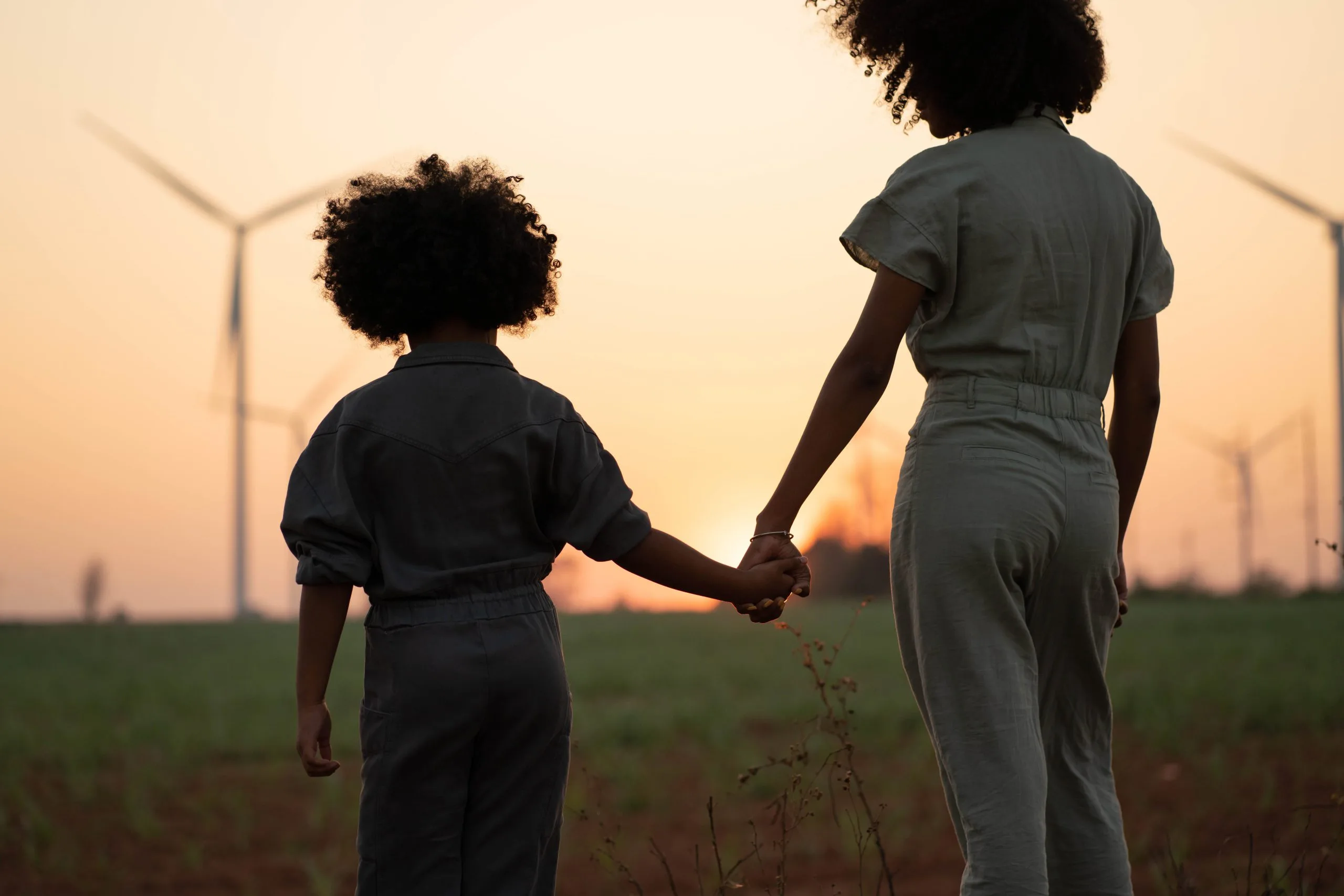 Two people silhouetted with wind turbines in the background