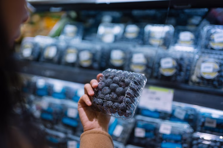 A grocery display of blueberries available with a single person making a selection.