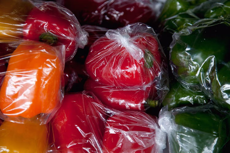 Close up photo featuring yellow, red, and green bell peppers wrapped in plastic bags.