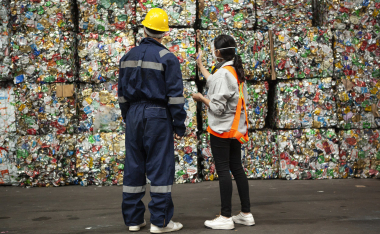 Male and female waste management workers standing in front of stacks of compacted recyclables