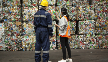 Male and female waste management workers standing in front of stacks of compacted recyclables.